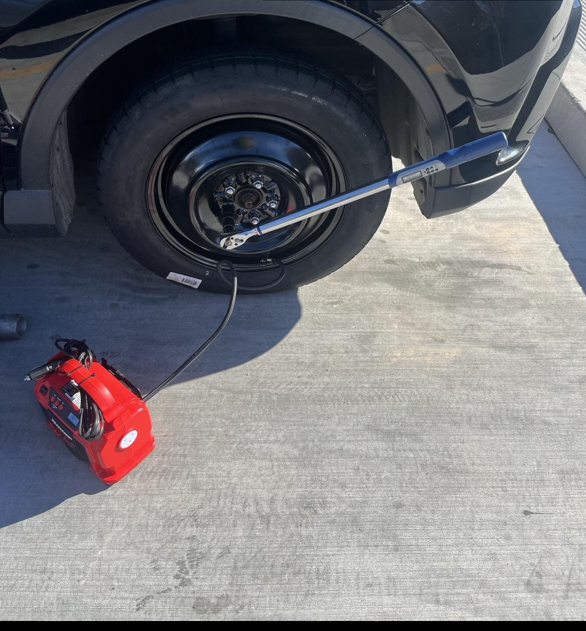Technician installing a customer's spare tire with a jack and impact wrench